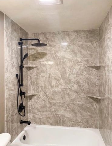 Elegant bathtub and shower combo featuring marble-look wall panels, matte black rainfall showerhead, and adjustable handheld
