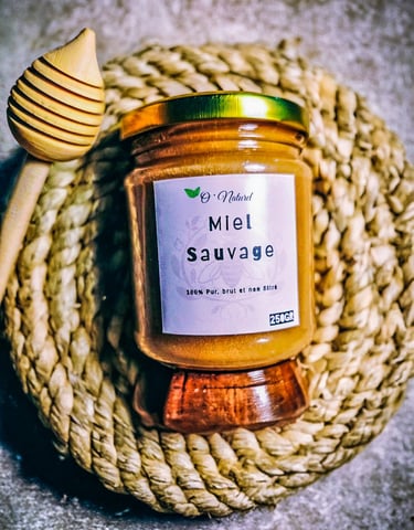 A glass jar of Miel Sauvage raw wild honey with a wooden dipper on a woven coaster.