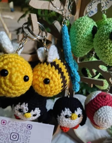 Llaveros de crochet amigurumi hechos a mano con abejas, pingüinos y hongos colgados en una exhibició