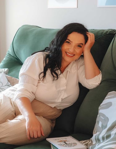 Raabe sentada em sofá verde sorrindo com caderno ao lado.