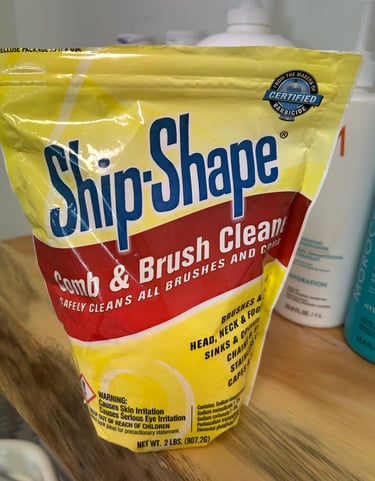 Ship-Shape Comb & Brush Cleaner 2 lb bag on a wooden vanity beside hair products.