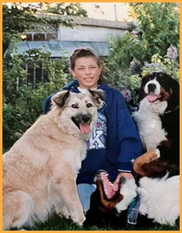Foto eines Jungen der im Gras sitzt und von Hunden umgeben ist