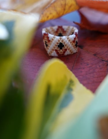 A ring made with Japanese seed beads on a table with some leaves around 