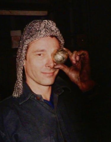 A portrait of Matt Carney holding a bronze world up to his left eye