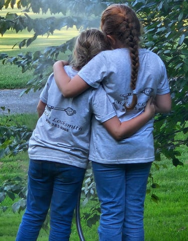 Two daughters hugging outdoors while wearing matching locksmith work shirts