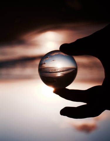 Des doigts tenant une boule de cristal reflétant avec clarté un coucher de soleil sur la mer