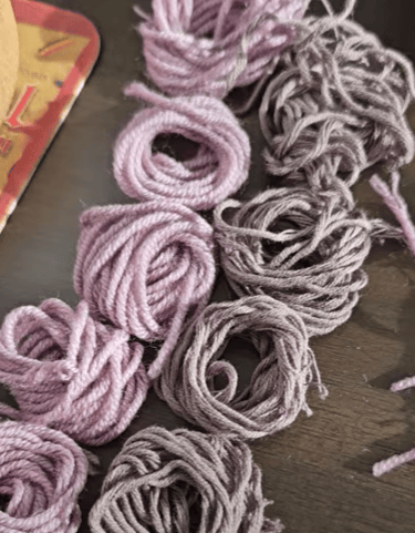 Small bundles of pink and brown wool yarn coiled on a dark wooden surface for knitting crafts.