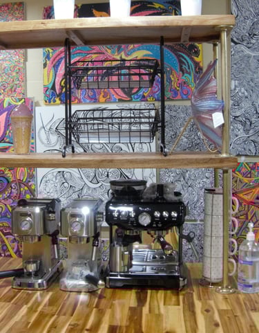 Coffee machines behind customer counter, with artwork by Chef Nick on wall behind them.