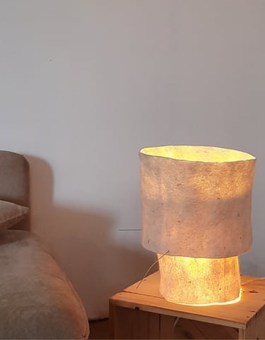 Handmade textile lamp glowing on a wooden side table next to a neutral couch.