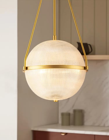 Modern gold globe pendant light with a textured glass shade hanging in a contemporary kitchen.