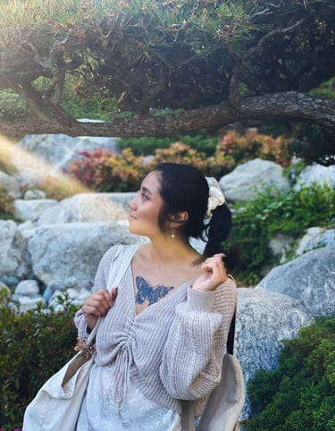 Me in a Japanese garden, holding ponytail looking left. Shows chest tattoo of a distorted butterfly.