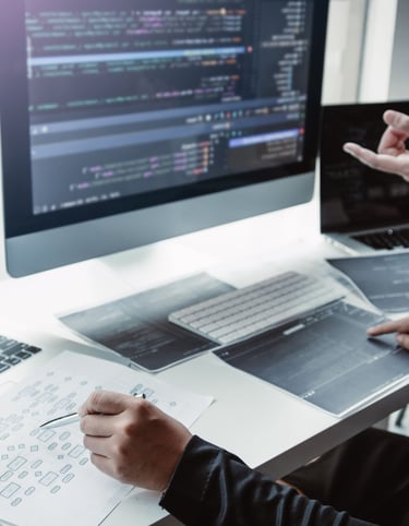 two people collaborating at a desk with laptops, a desktop and printouts