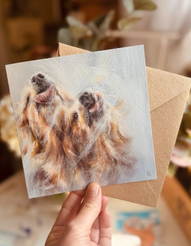 A square shape greeting card featuring a design of two golden retrievers playfully licking a window