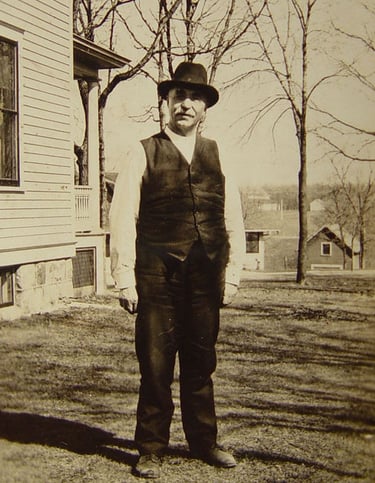 a gentleman in a vest and hat standing outside a house, black and white