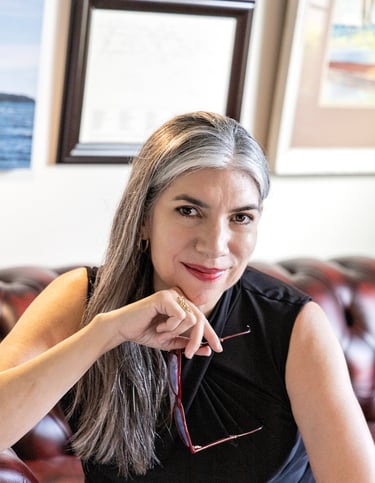 Poet Sheena Powell seated and smiling, with long silver-streaked hair, wearing a black sleeveless top