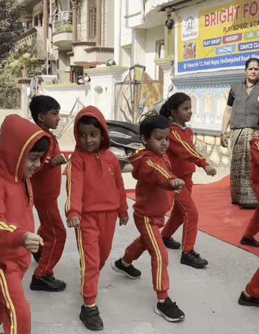 Preschool children in red tracksuits practicing a march outside Bright Foster Kids school in India.