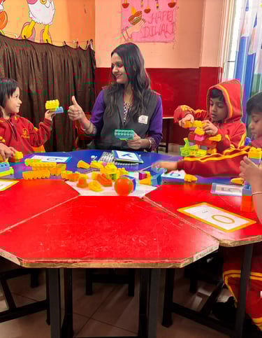 Preschool children in red uniforms building with colorful toy blocks around a table with their teacher.