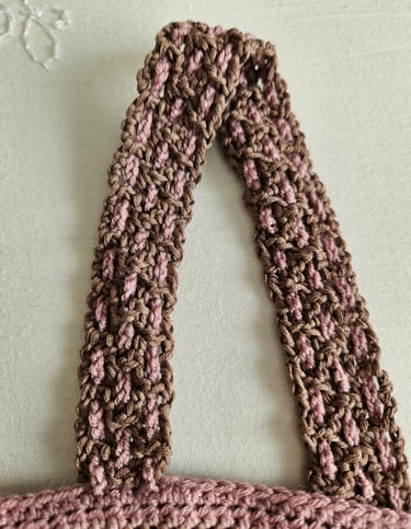 Close-up of a brown and pink crocheted shirt strap featuring a filet crochet pattern.