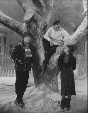 Busby Berkeley advising Ruby Keeler and Dick Powell while sitting in a snowy stage prop tree.