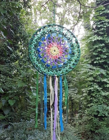 Dreamcatcher, hvatač snova nastao reciklažom plastičnih kesa, visi u zelenoj šumi. Simbol VATRE.