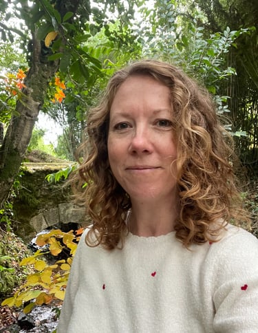 photo of Iona Reading wearing a cream jumper standing in front of a stream surrounded by trees