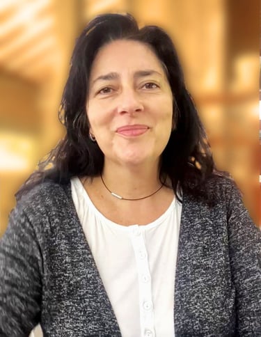 Smiling woman with long dark hair wearing a grey cardigan and white blouse in a professional setting.