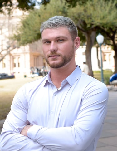 Professional portrait of a man with arms crossed in a white shirt at the Texas Capitol building.
