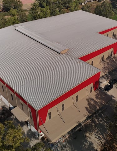 Aerial view of a modern industrial warehouse building with a red and beige exterior and corrugated metal roof.