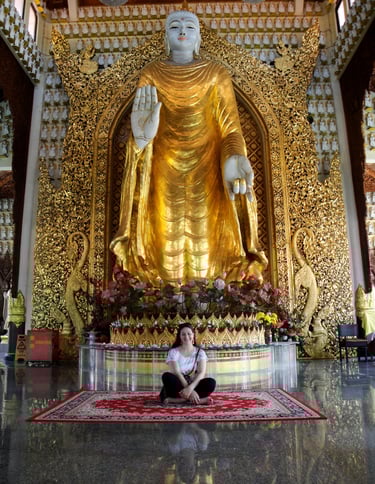 foto da autora sentada no templo abaixo das mãos de buda em penang malasia