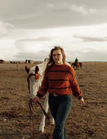 a woman in a red sweater and jeans walking with a horse