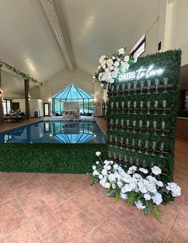 Wedding champagne wall set up with a cheers to love neon with white roses and greenery