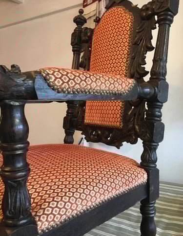 Fauteuil en bois foncé recouvert d'un tissu à motifs rouge et jaune agrémenté de clous décoratifs