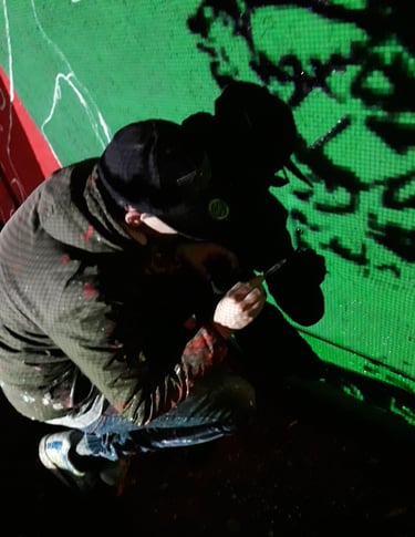 Artista al lavoro durante la realizzazione di un murales su fondo verde, pittura murale notturna