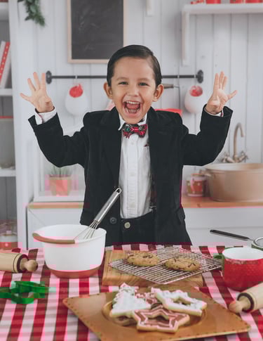 un niño con smoking sonriendo a la cámara frente a galletas navideñas
