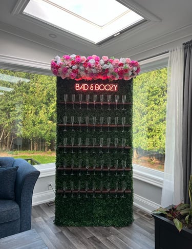Champagne wall of assorted pink roses and a sign that says bad & Boozy