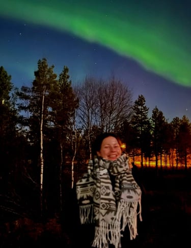 a woman standing under the northern lights with a smile