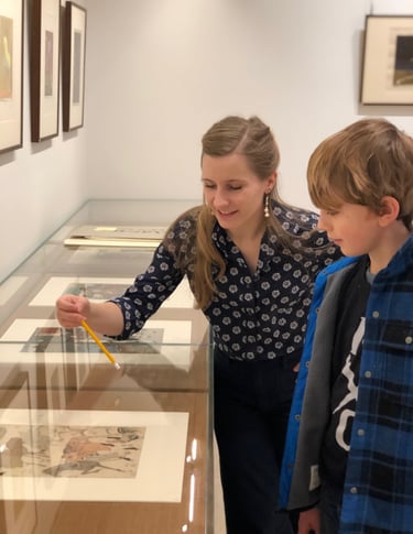 Madison points to a japanese print in the vitrine as she teaches a child in a gallery setting