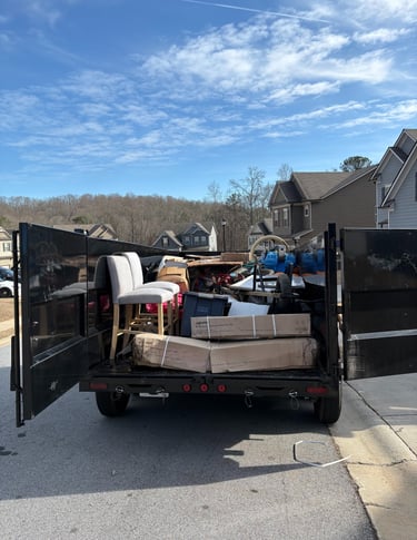 A black junk removal trailer filled with furniture, boxes, and debris for residential waste disposal.