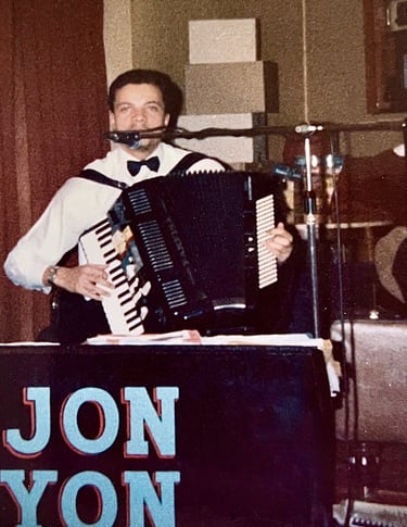 Jon Yon playing and singing live with his electronic accordion, surrounded by a stack of speakers.