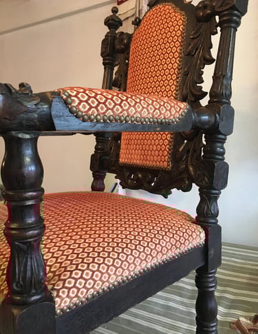 Fauteuil en bois foncé recouvert d'un tissu à motifs rouge et jaune agrémenté de clous décoratifs