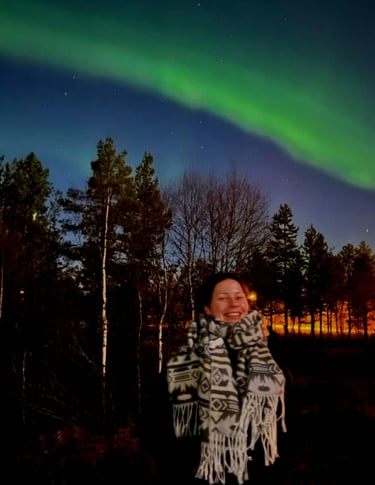 a woman standing under the northern lights with a smile