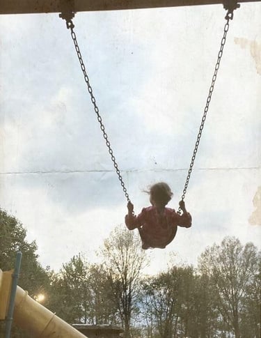 Girl swinging on a playground with trees in the background