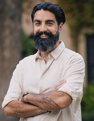 Eamon Moghimi smiling with arms crossed in a light shirt standing outdoors in a calm natural setting