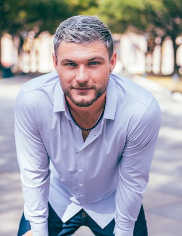 Young man with silver hair and a beard wearing a white button-down shirt outdoors.