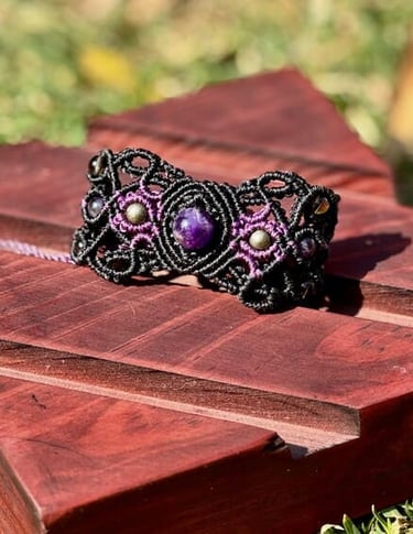 Pulsera de macramé artesanal en negro y morado con amatistas, exhibida sobre un soporte de madera.