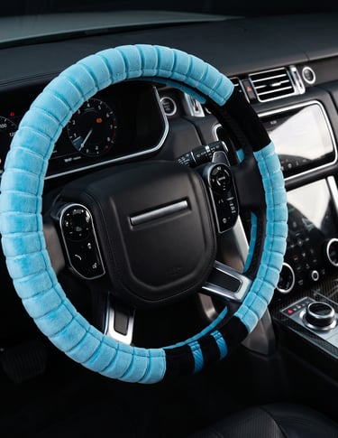 A soft light blue plush steering wheel cover installed on a black luxury SUV interior dashboard.