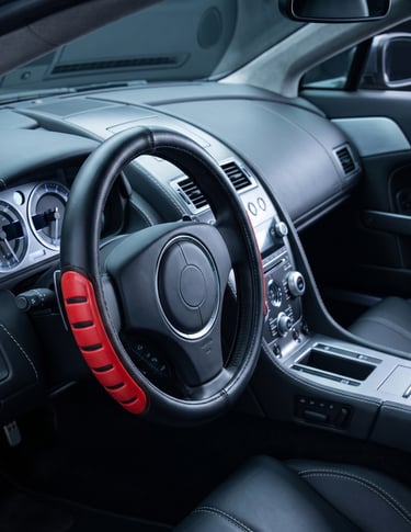 Luxury car interior featuring a black leather steering wheel with a red and black grip cover.