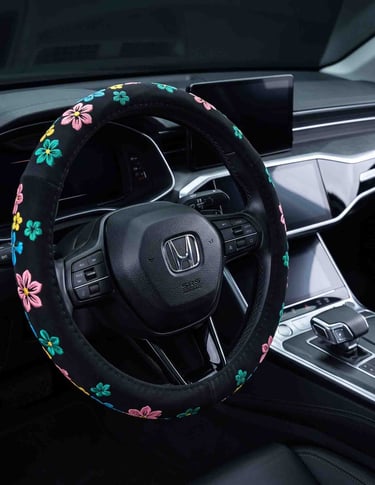 Black suede steering wheel cover with colorful embroidered flowers inside a modern car interior.