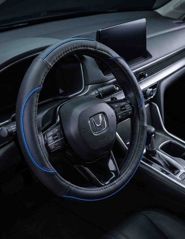 Black leather steering wheel cover with blue trim installed in a modern car interior dashboard.