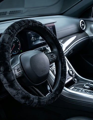 Soft blue and black fuzzy steering wheel cover on a black luxury car interior, enhancing grip and comfort.